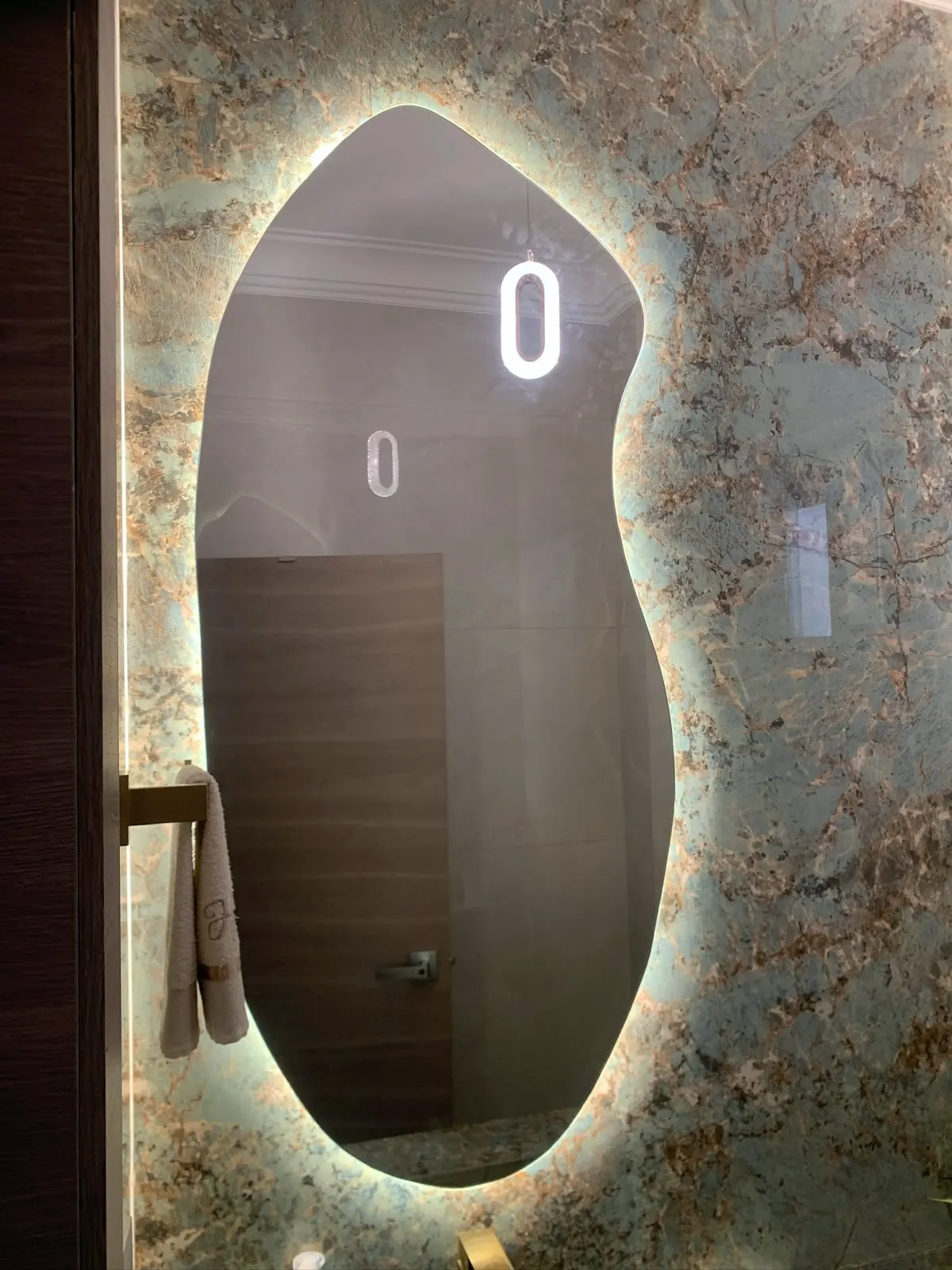 Espejo orgánico retroiluminado sobre una pared de ónix veteado, en un baño social