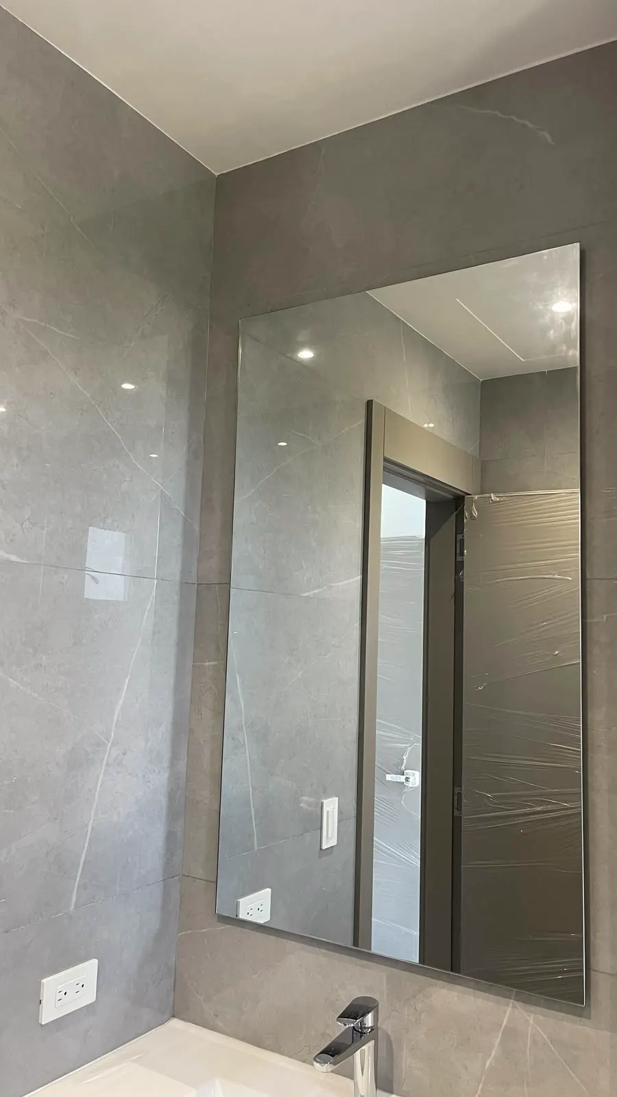 Espejo de gran formato sin marco en un baño gris, del ancho completo de la pared