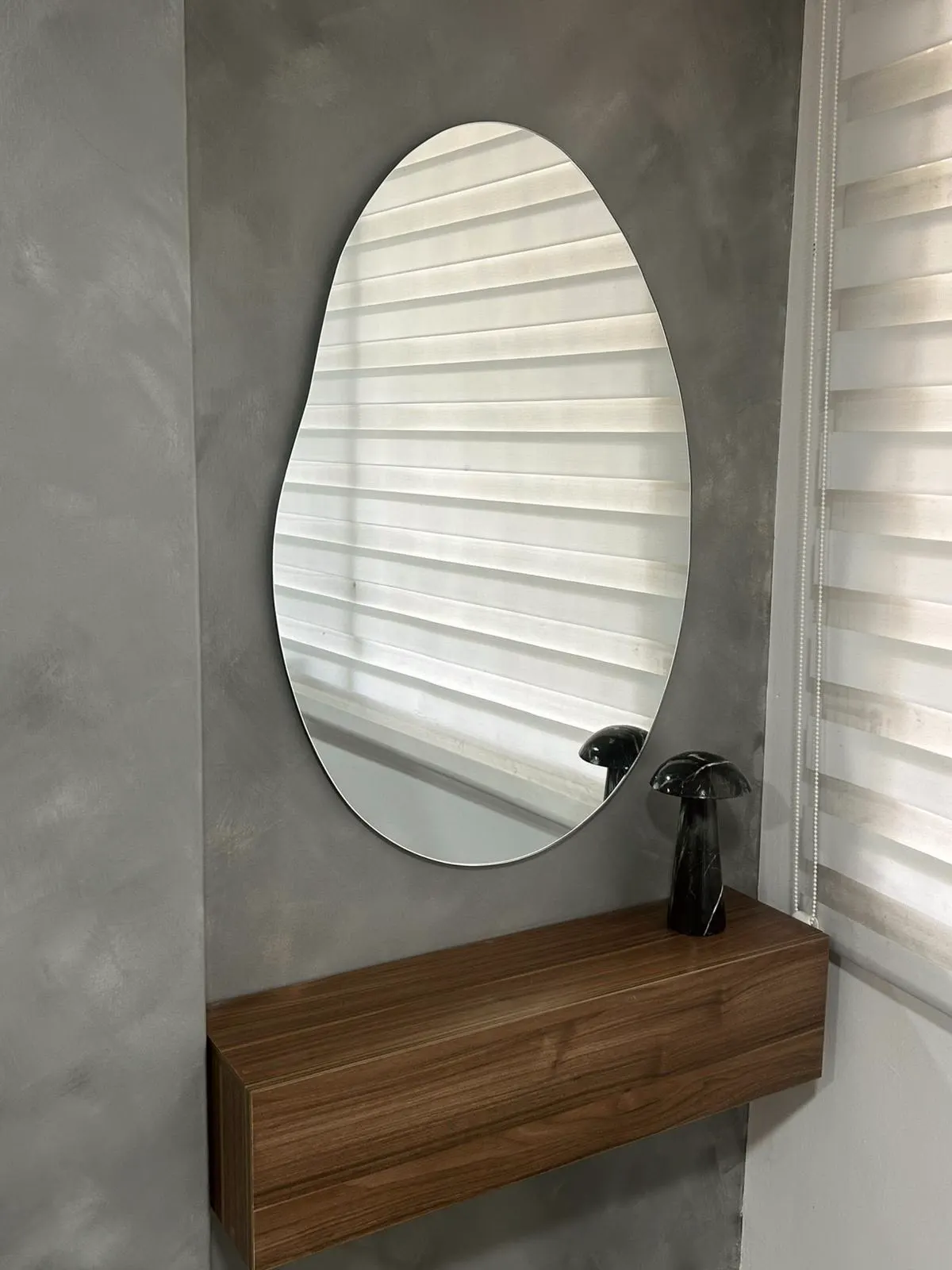 Espejo orgánico sobre pared de microcemento, con repisa flotante de madera