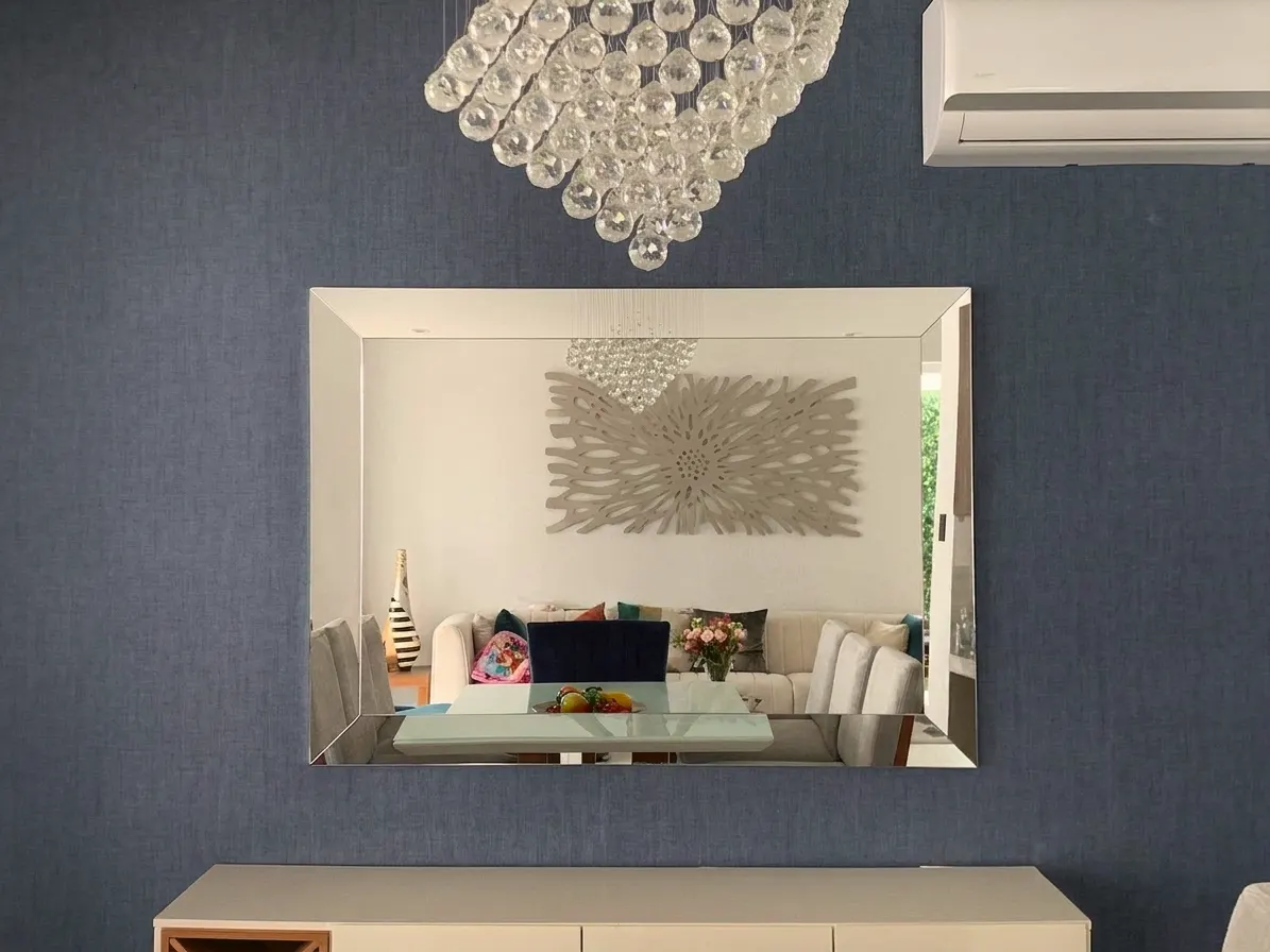 Espejo de marco espejado sobre pared azul, con lámpara de cristal y mueble bajo