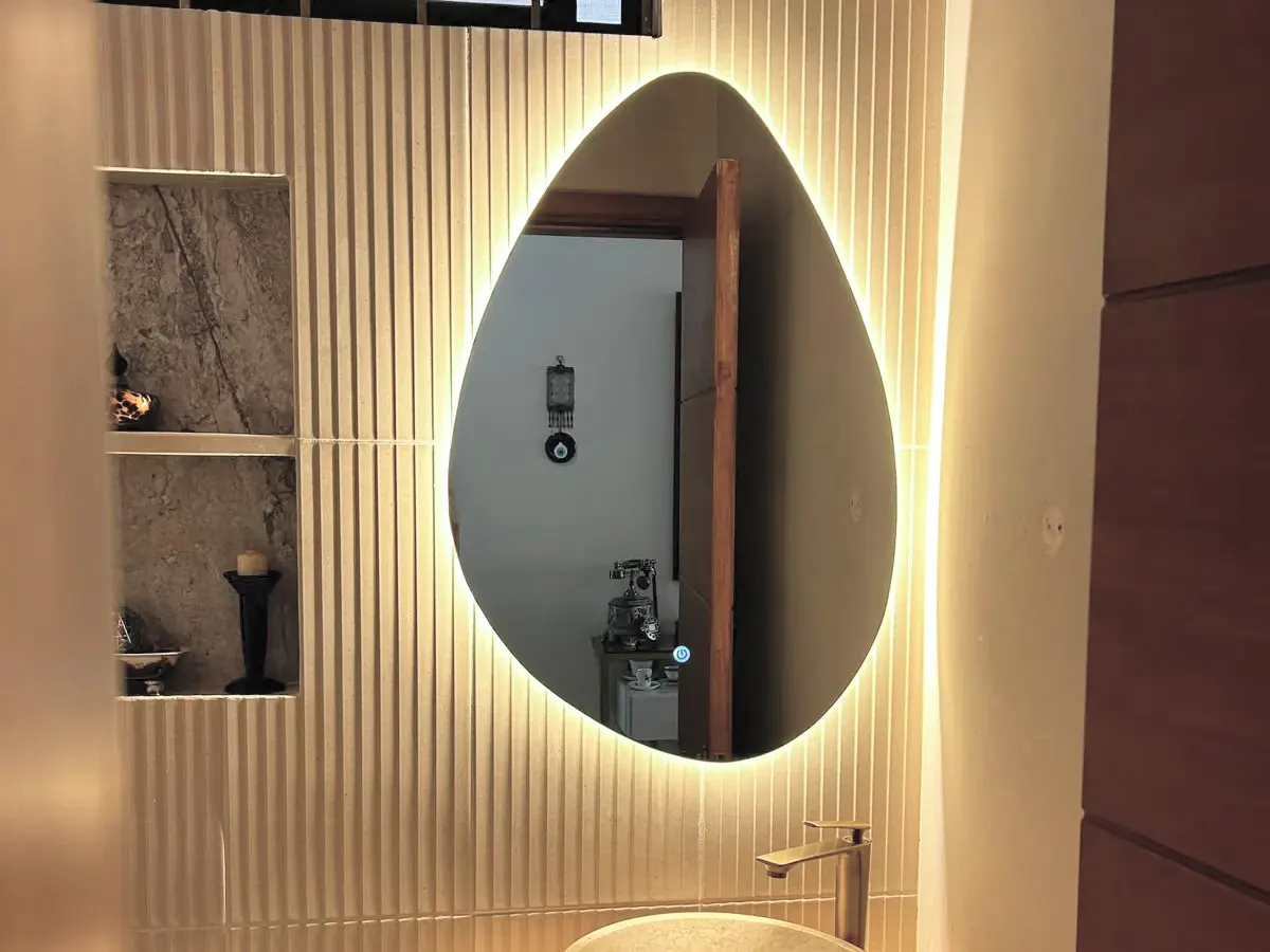 Espejo orgánico retroiluminado sobre un panelado acanalado, con la luz rebotando en la pared