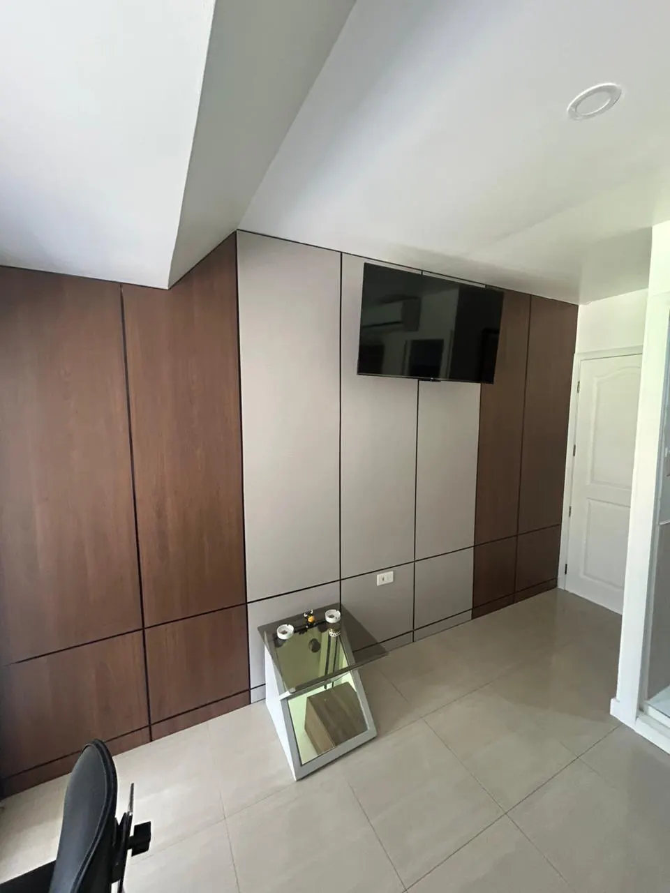 Pared revestida de paneles en dos tonos, madera oscura y beige claro, con juntas finas y un televisor montado al centro