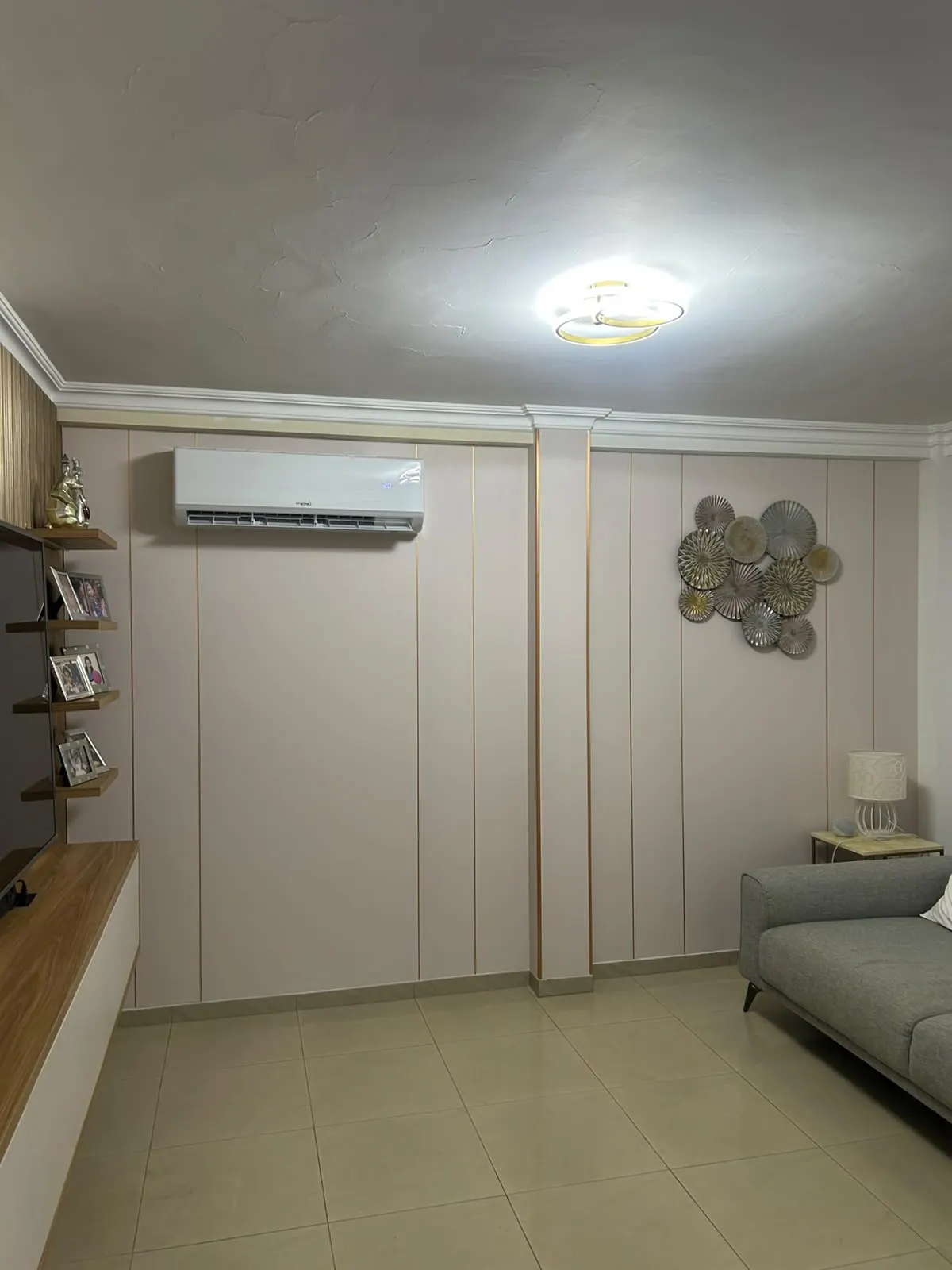 Paneles decorativos de listón claro con filete dorado cubriendo la pared de una sala, junto a un mueble de televisión de madera
